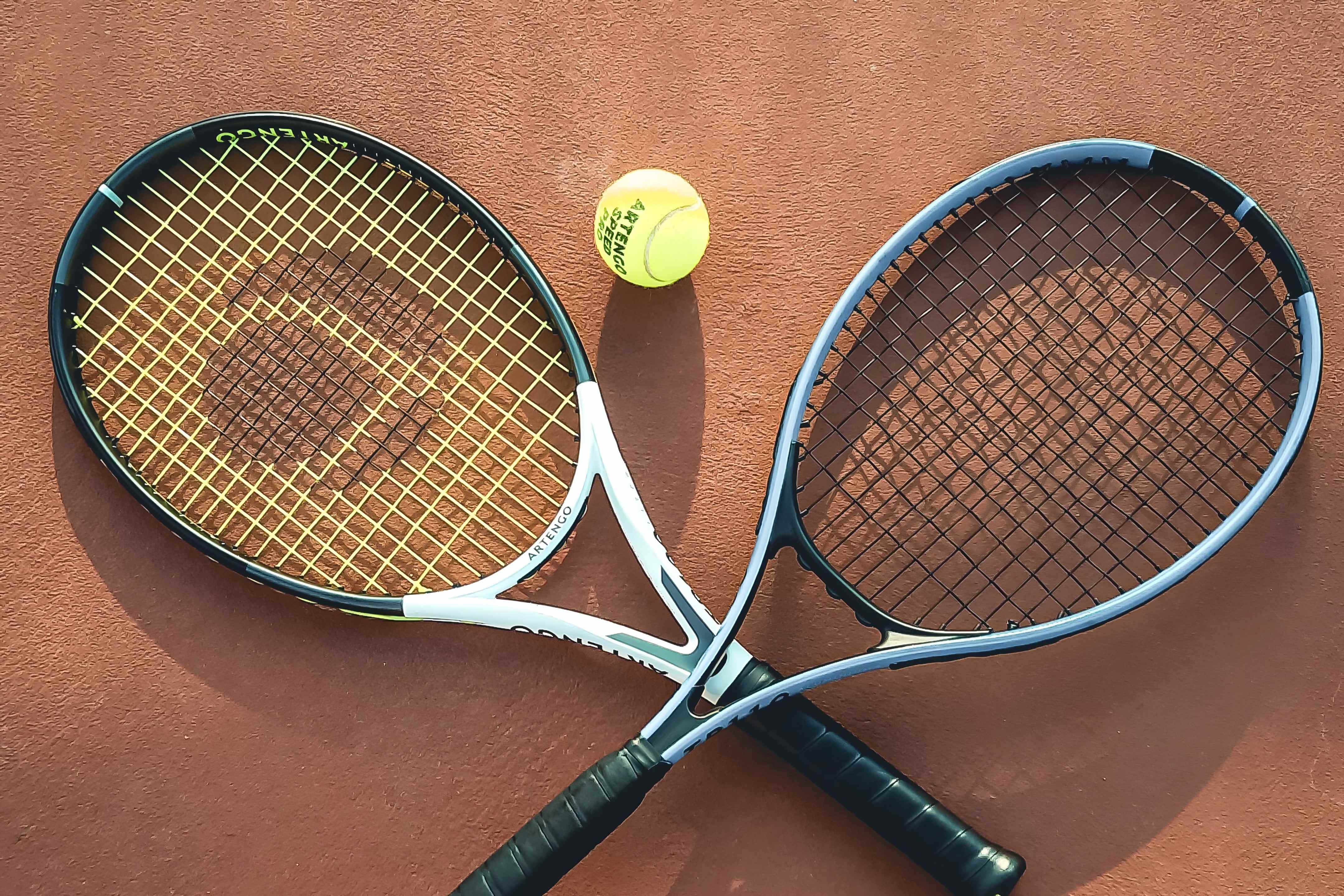 Deux raquettes croisées et une balle posées sur un court en terre battue