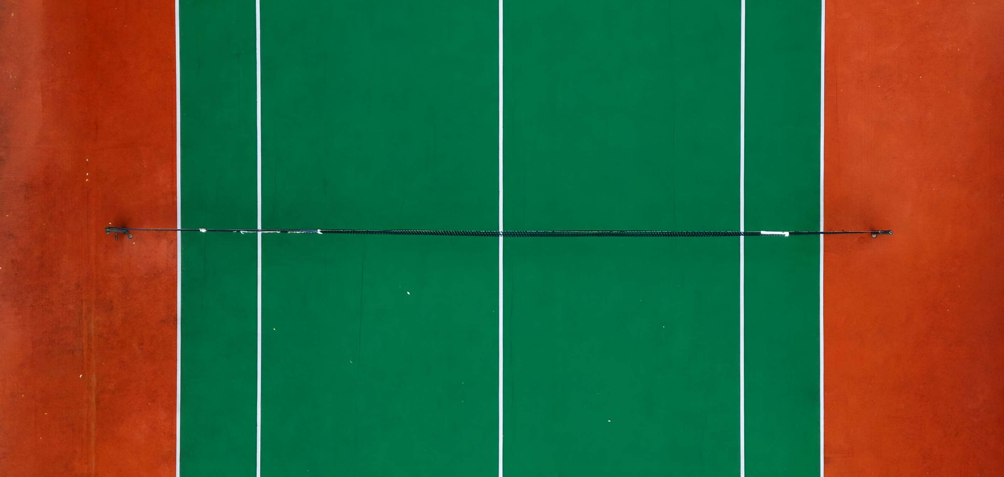 Surface d’un court de tennis vert traversée par une ligne blanche