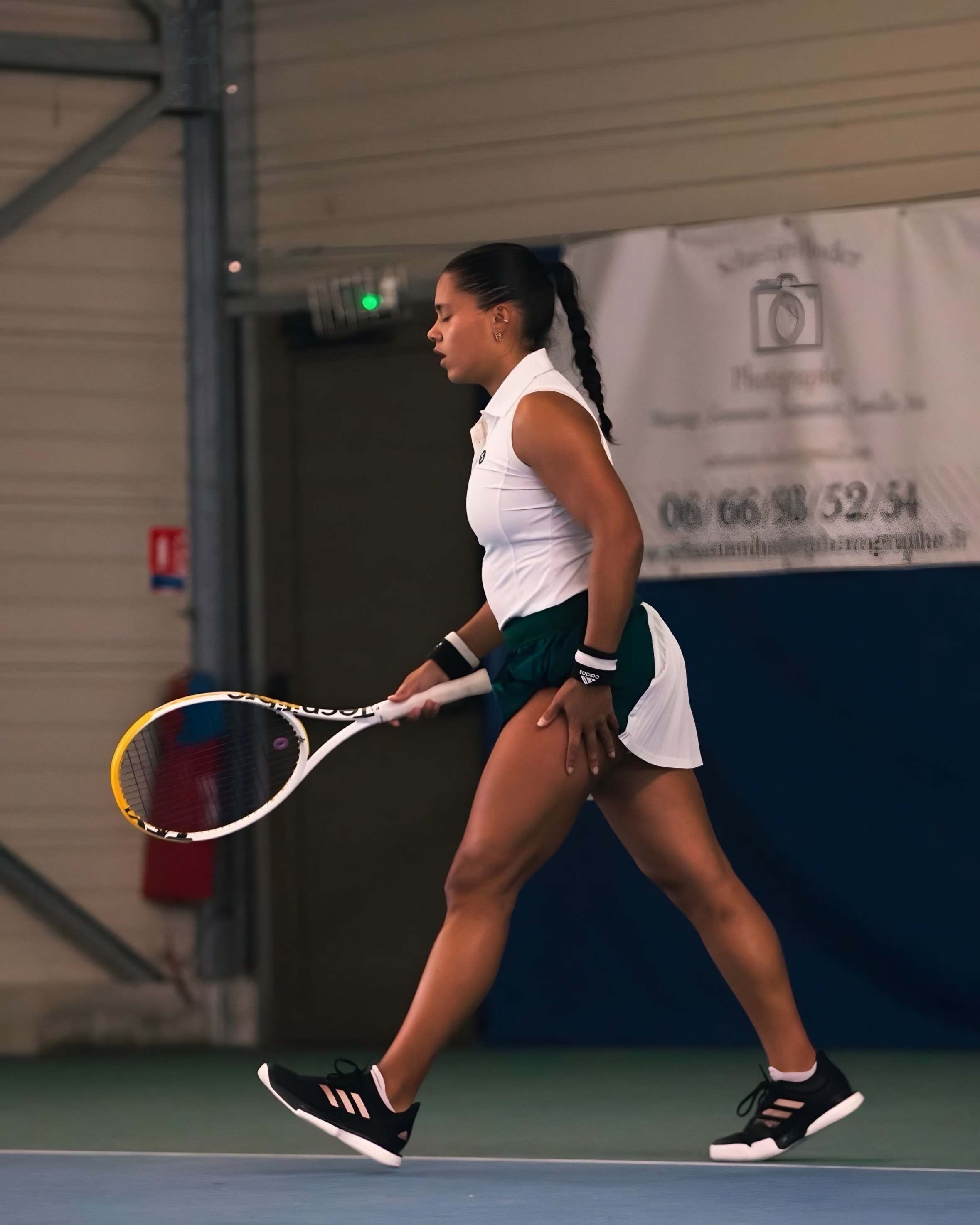 Jade entre deux points sur un court couvert, la main posée sur la cuisse