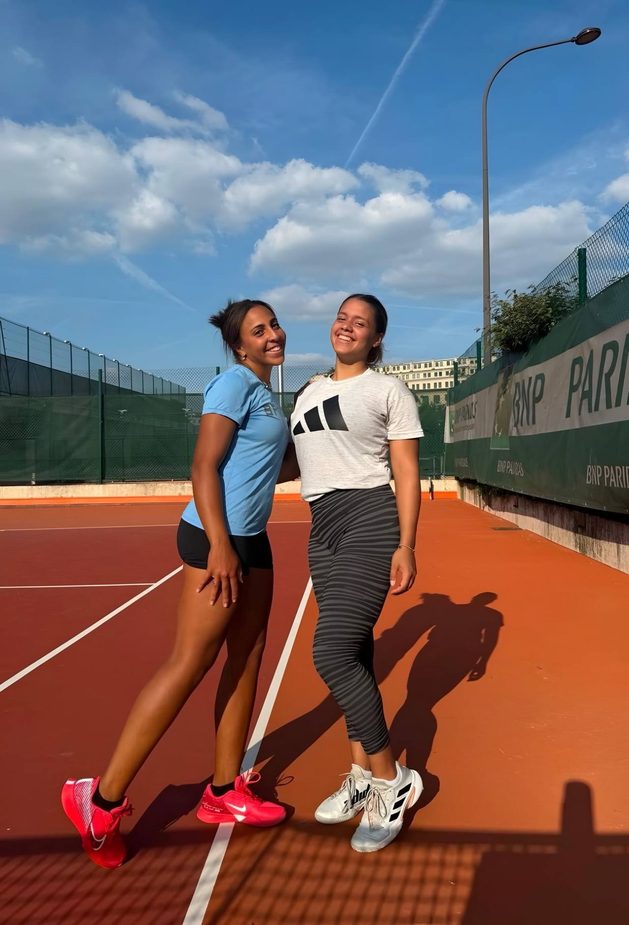 Sophia et Jade côte à côte sur un court en terre battue, sous un ciel bleu